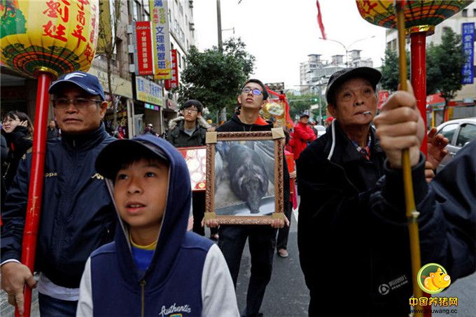 特等奖得主刘进生退休前在桃园客运开了23年公车，每逢初一、十五都会到清水祖师庙拜拜，祈求祖师公、关圣帝君保佑他行车平安；3年前退休，为感谢清水祖师庙多年保佑，决定在刘姓值年时养大猪公酬神。图为获奖神猪的家人抱着该猪的画像参加游行。